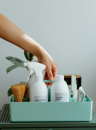Hand arranging cleaning products in a tidy organizer, promoting cleanliness and order.